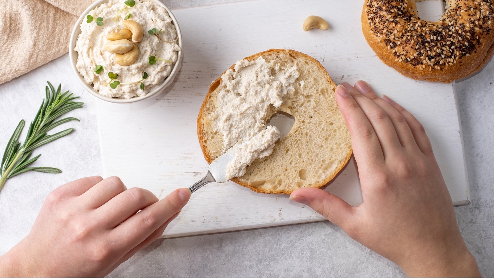 female-hands-spreading-cashew-cheese-on-a-bagel-2021-12-17-00-58-57-utc